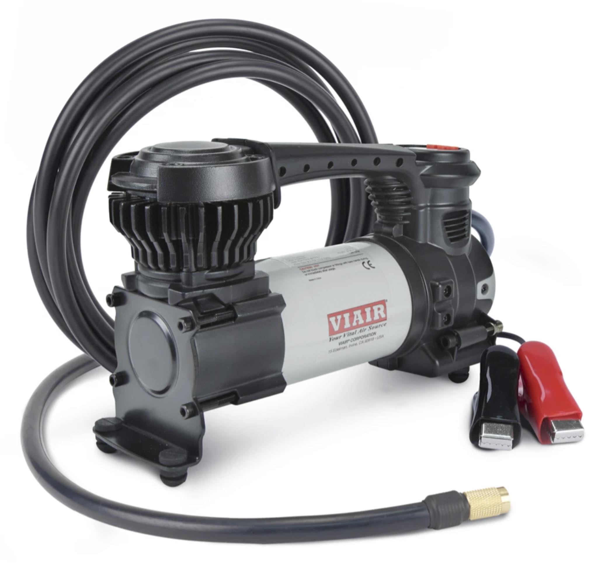 Close-up of a gray air compressor with a thick black hose looped over it and a red handle visible on the side against a white background.