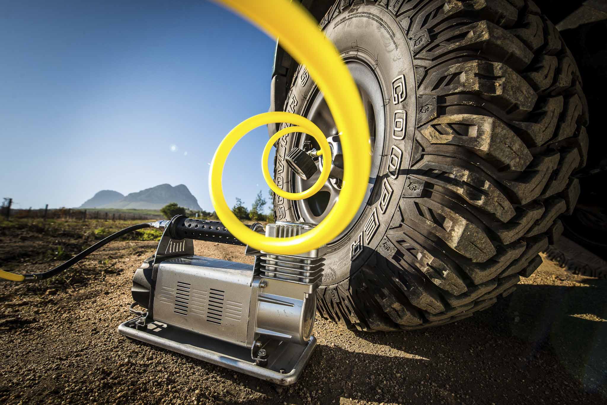 Off-road vehicle tire with a bright yellow air hose looping around a winch in a desert setting.