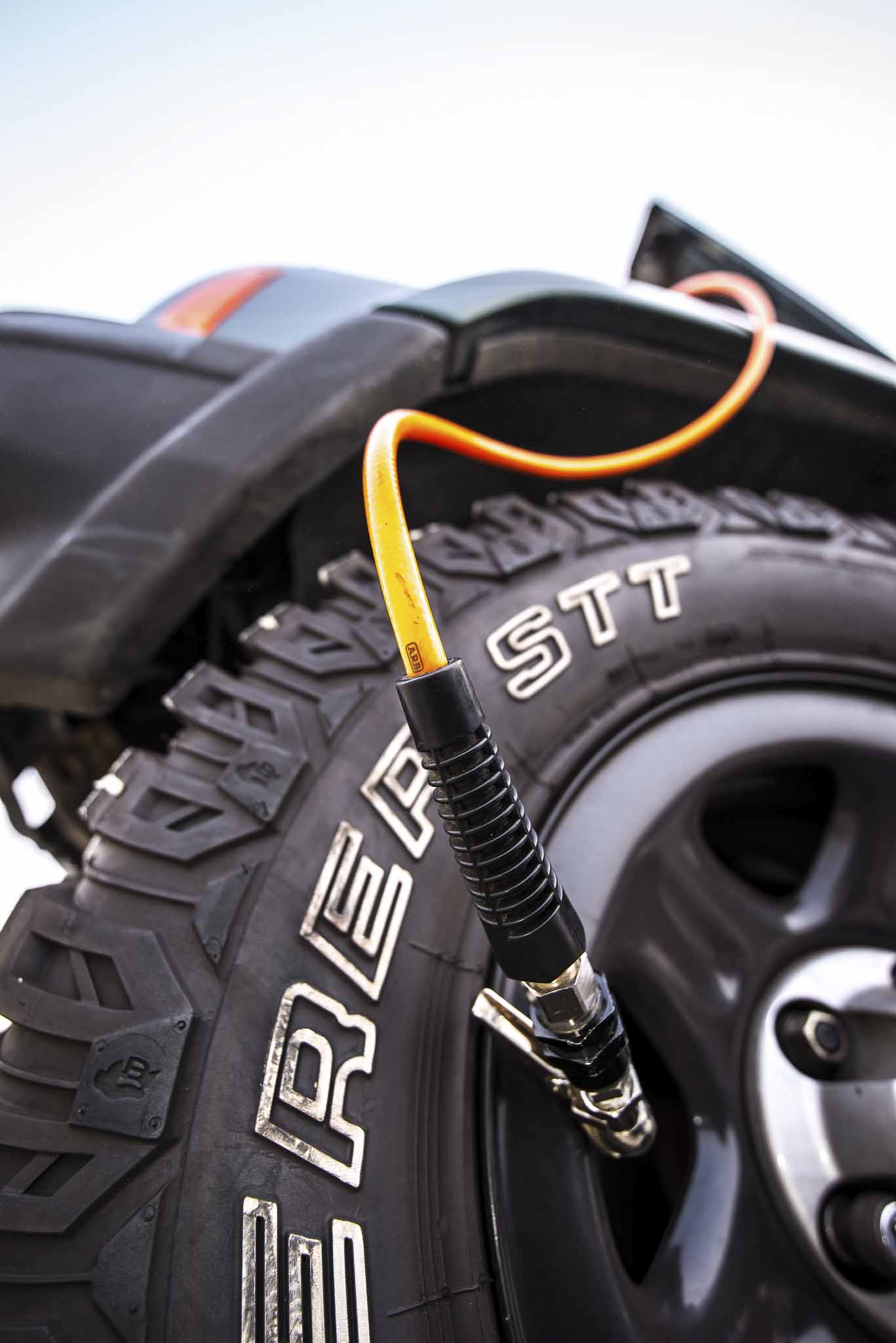 Close-up of a rugged off-road tire with a bright orange bicycle pump hose connected to the valve.