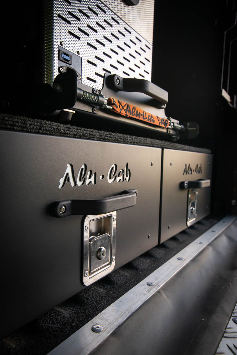 Close-up of a metal flight case with black handles and silver latches in a truck bed or cargo area.