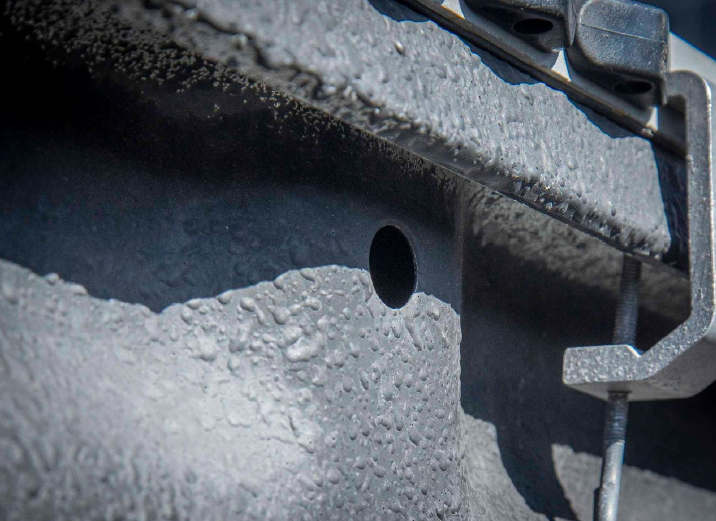 Close-up of a rough gray metal surface with a circular hole and a nearby clamp holding a cable.
