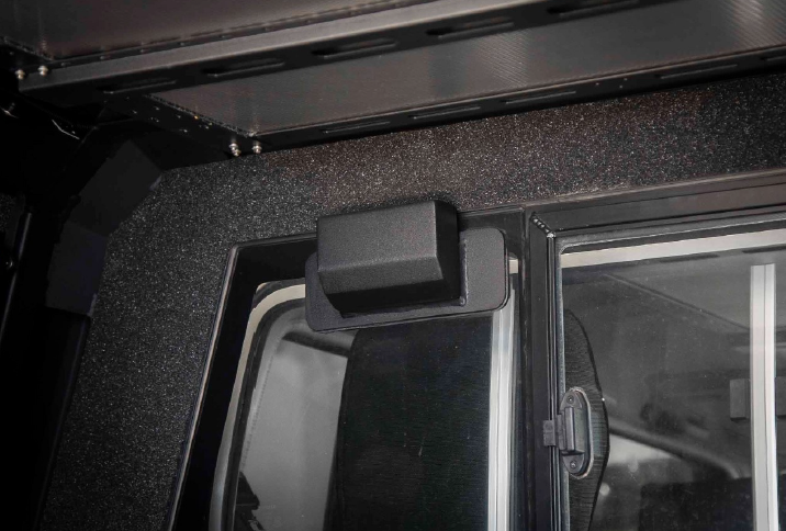 Close-up of a black rectangular fixture mounted on top of a truck cab door, with foam-lined frame and dark glass nearby.