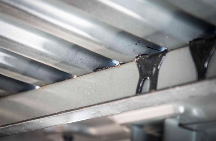 Close-up of a corrugated metal roof seam with black sealant dripping from a joint.